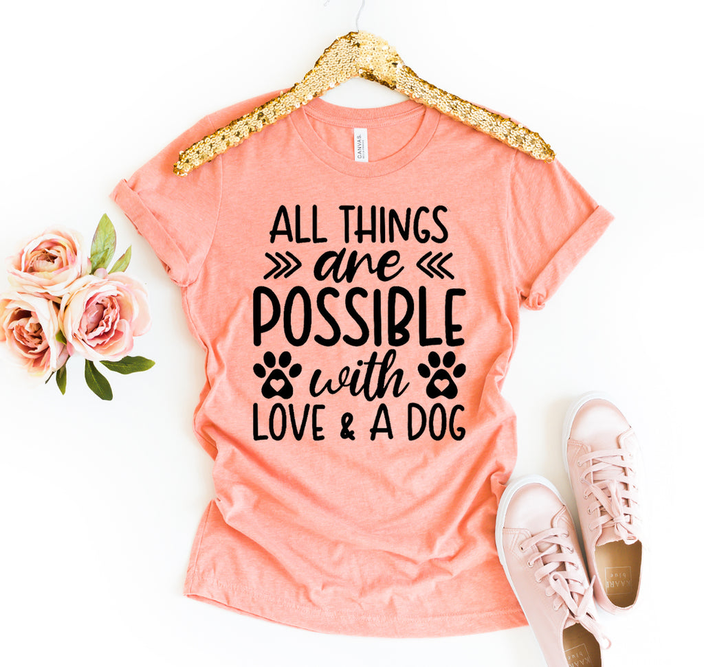 Coral t-shirt with motivational quote on a hanger with gold trim, next to pink sneakers and flowers.